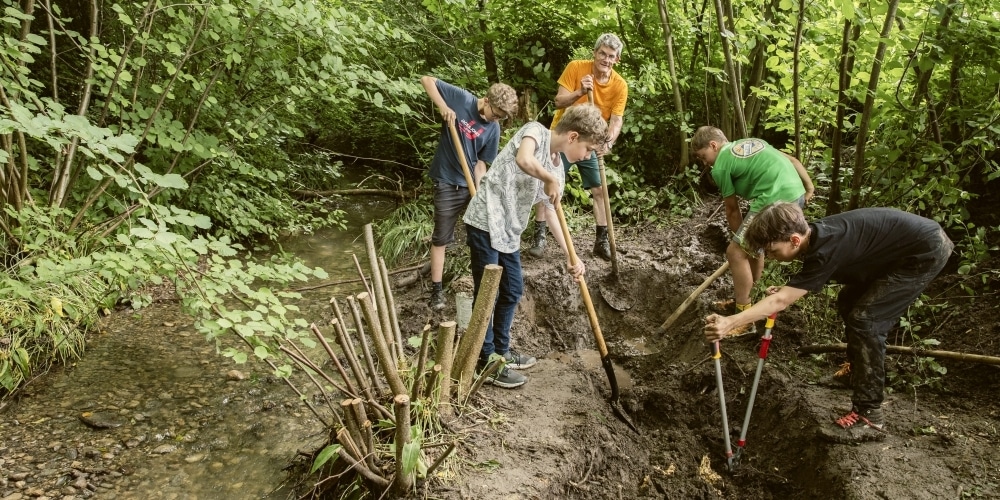 Primarschüler bauen unter Anleitung ihres Lehrers im Wald einen Tümpel.